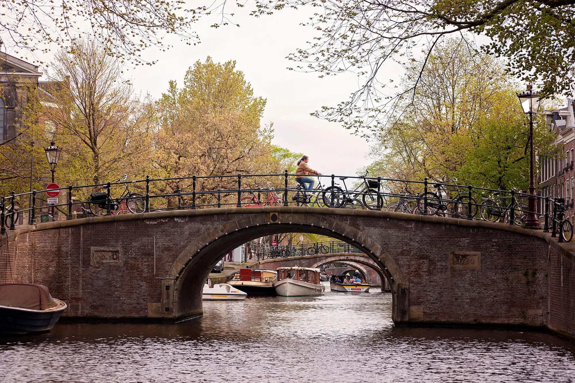 A cyclist crosses a historic bridge over Amsterdam's scenic canals, capturing the essence of city life.