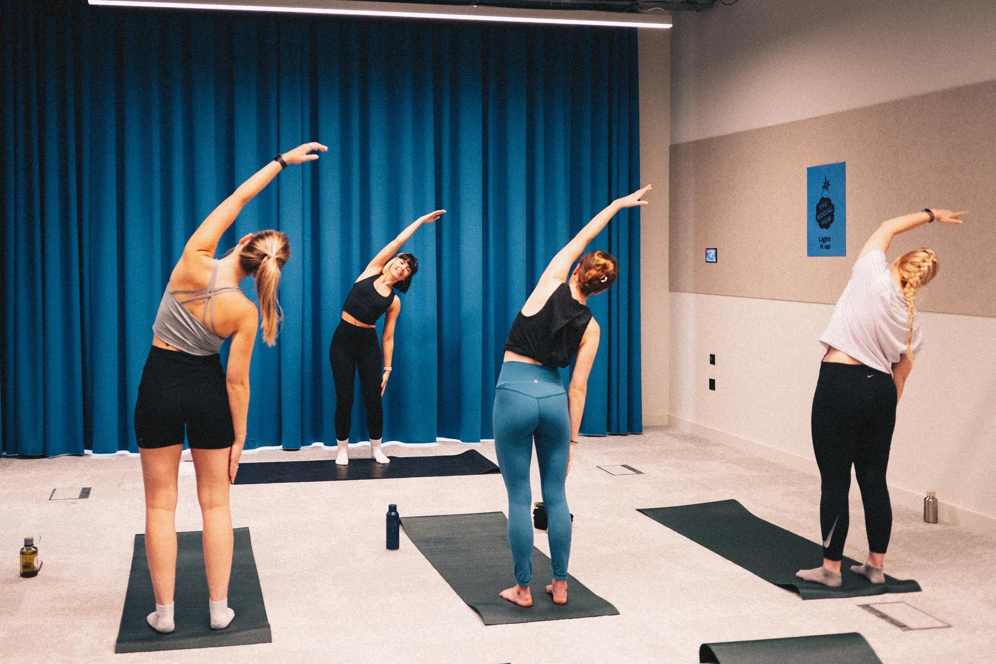 Four people in athletic wear practice side-stretch yoga poses on individual mats in a studio.