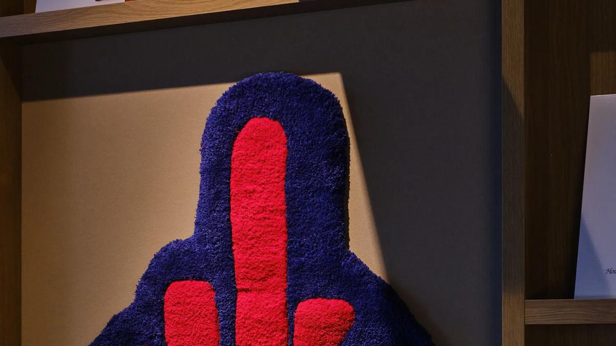 A decorative wall piece shaped like a raised middle finger, with the words fuck you in red letters on a blue background.