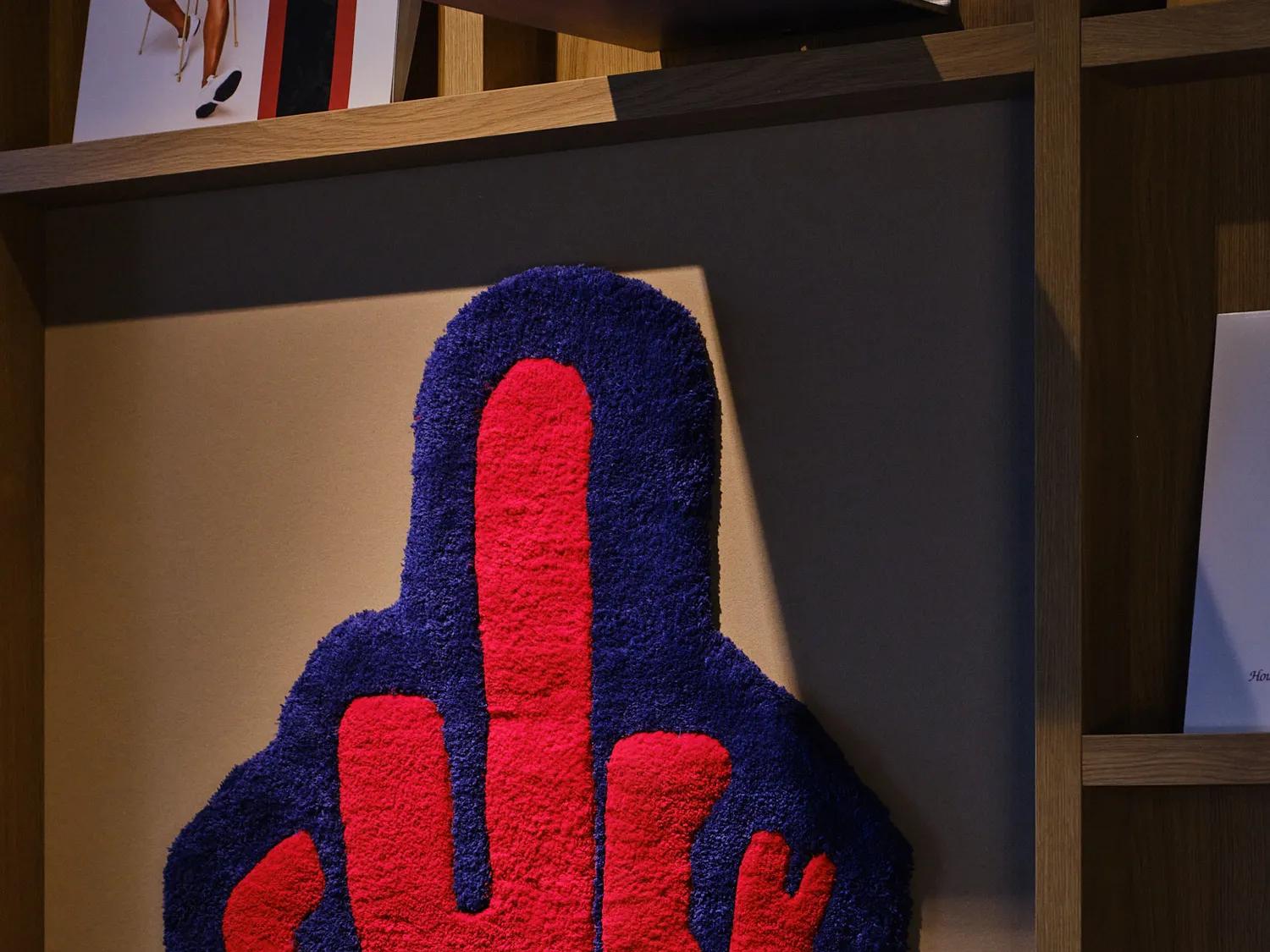 Une décoration murale en forme de doigt d'honneur, sur laquelle figurent les mots « fuck you » en lettres rouges sur fond bleu.