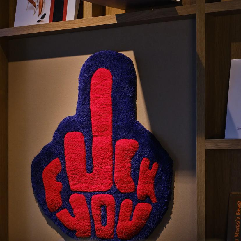 A decorative wall piece shaped like a raised middle finger, with the words fuck you in red letters on a blue background.