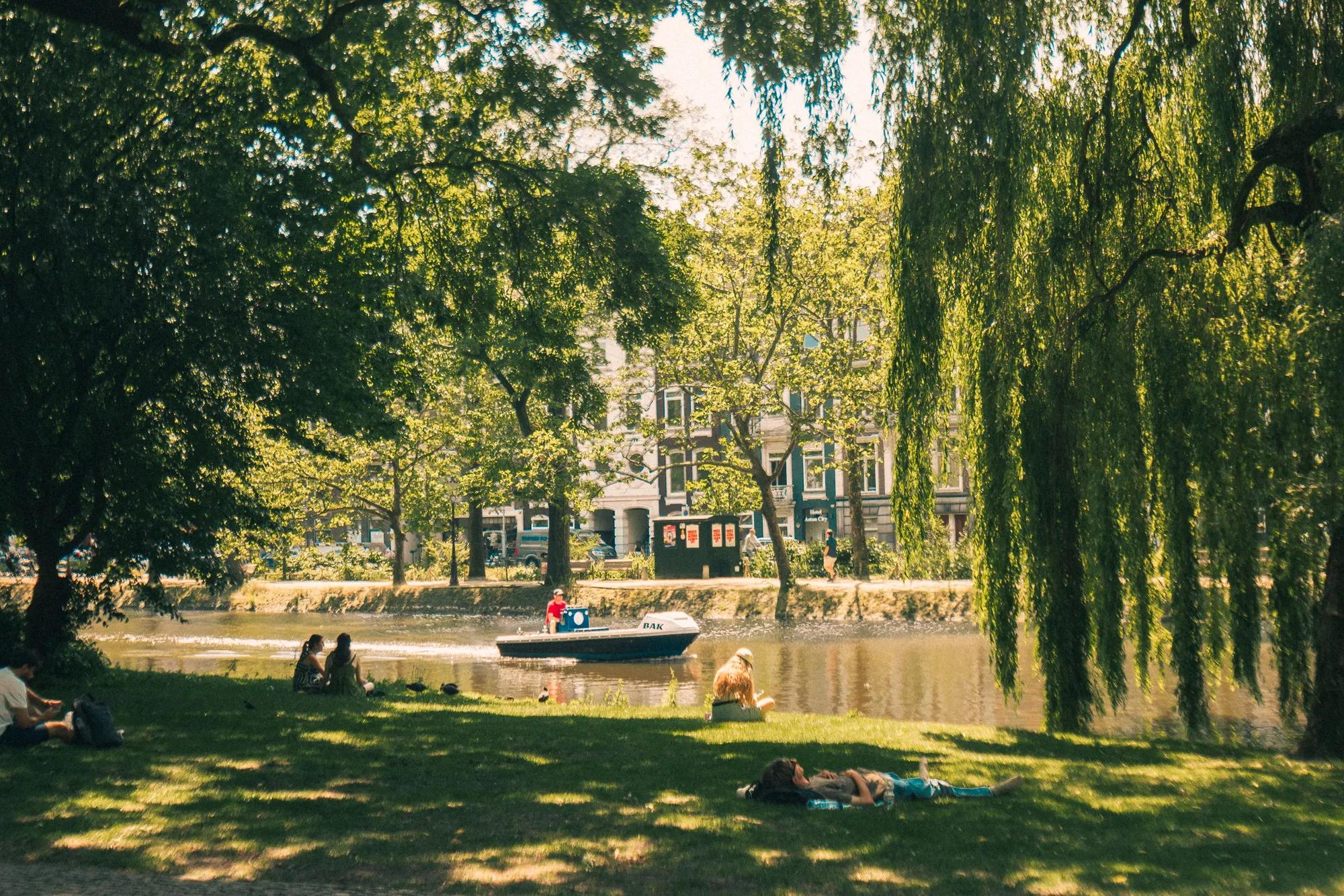 Serene summer scene with people relaxing by an Amsterdam canal under lush greenery.