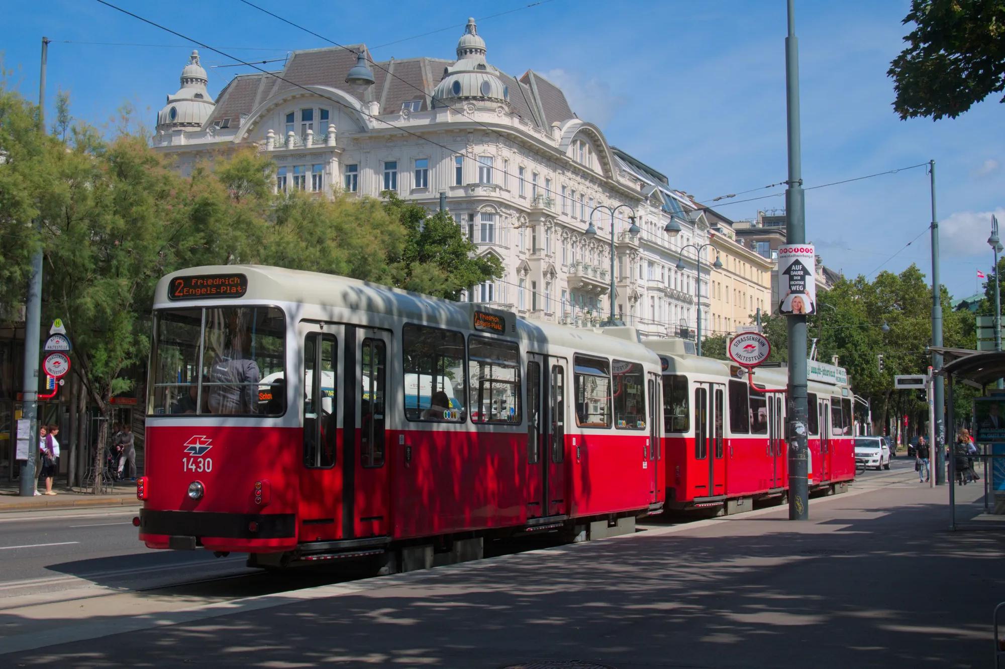 Iconic red tram traverses scenic city streets of Vienna, Austria against a bright blue sky.