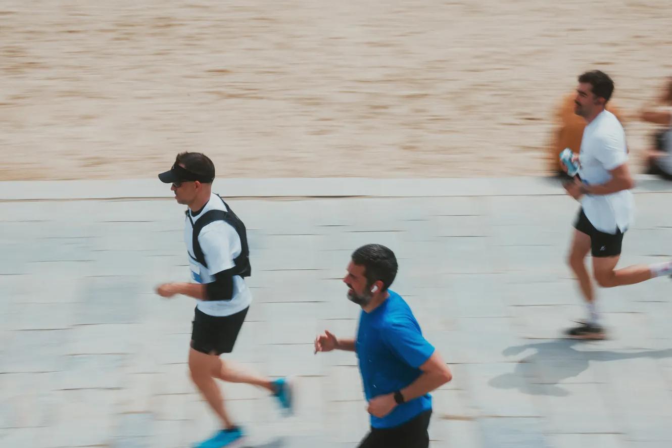 Three people running along a paved path next to a sandy beach.