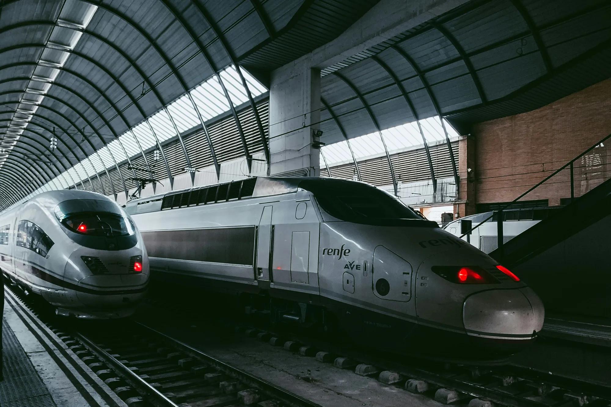 A silver train traveling down train tracks next to a loading platform.