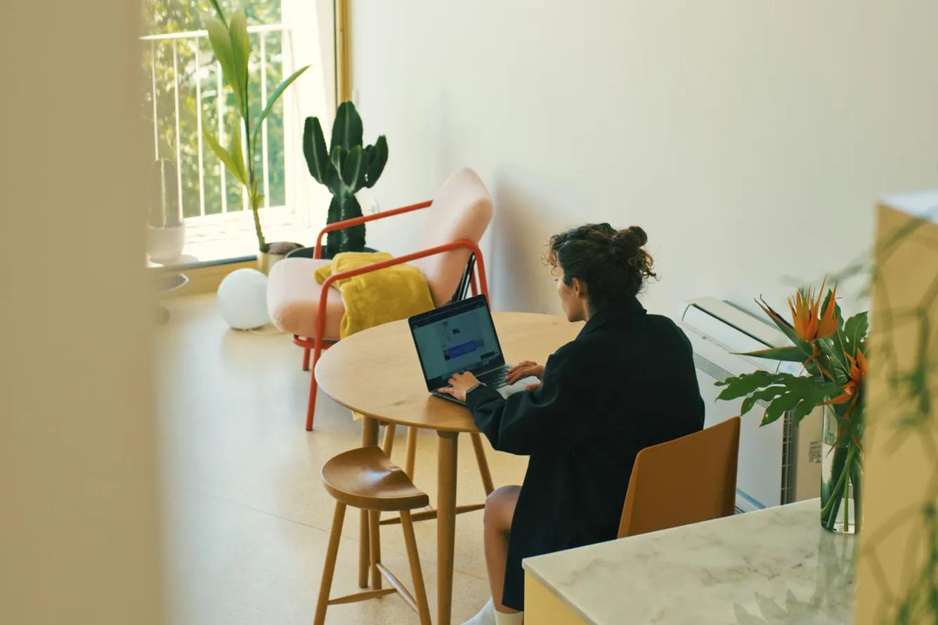Curly girl sitting at the table with a laptop surrounded with plants.